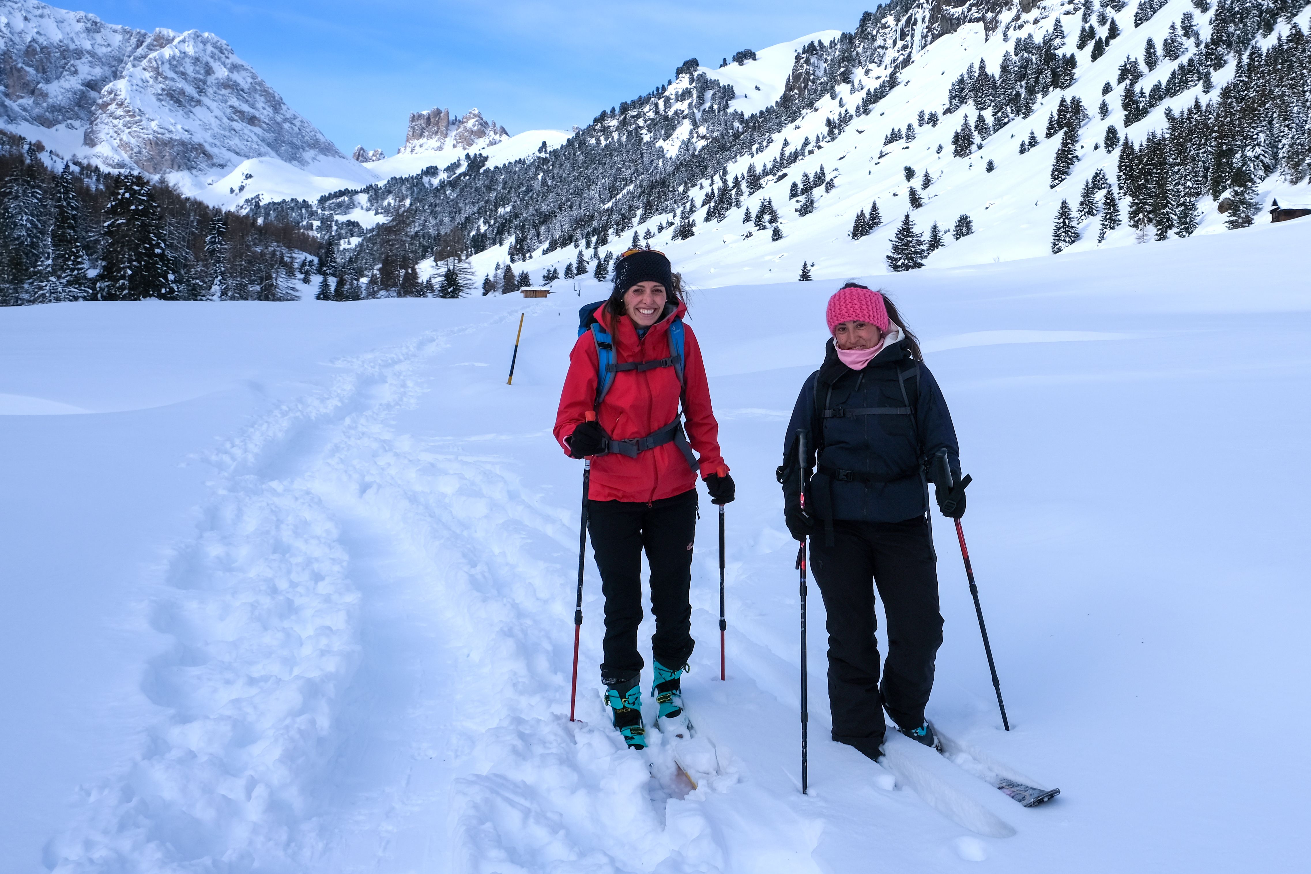 Two ladies walking in the snow with skis and poles