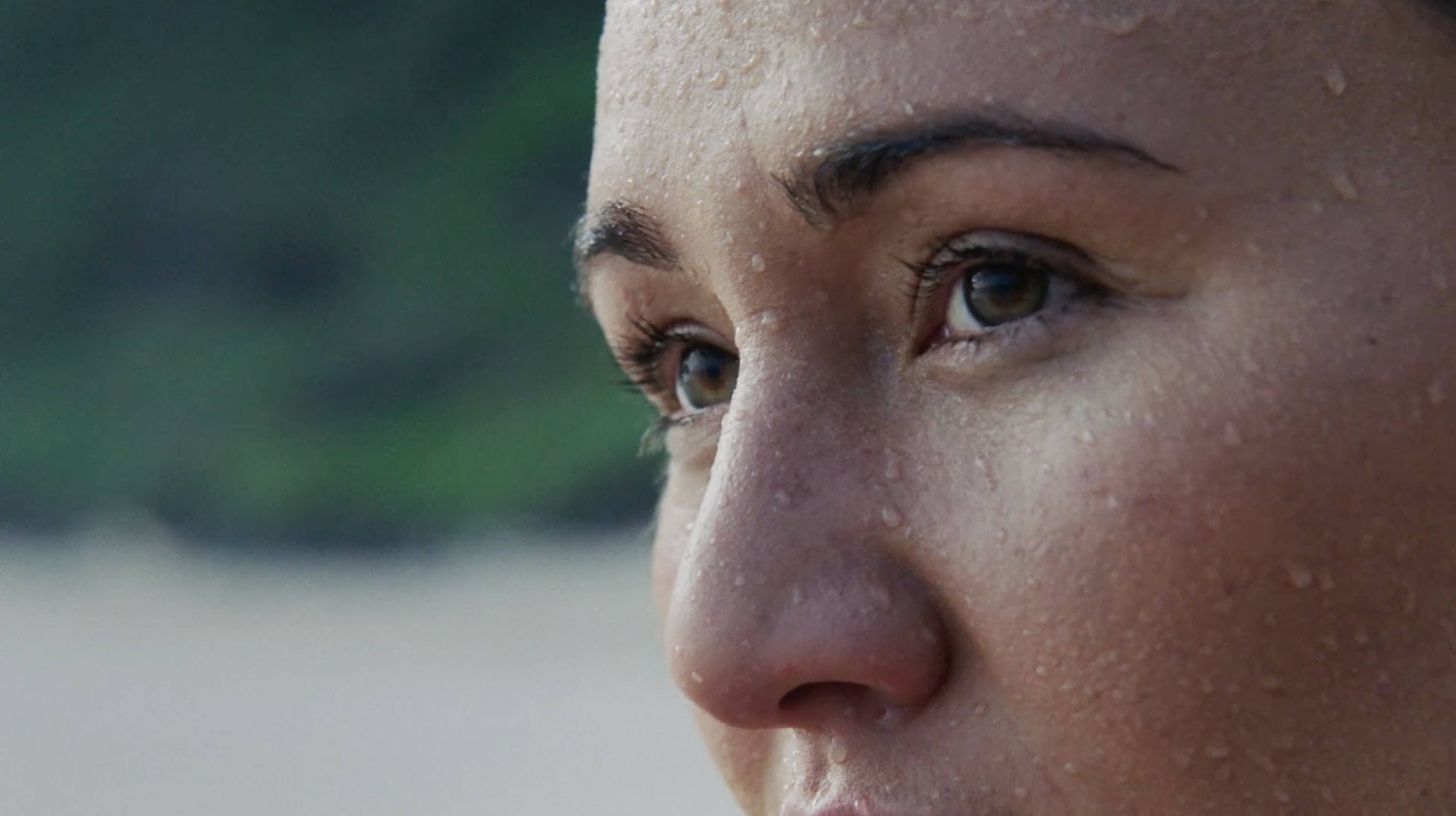 Close-up of a woman's face with water droplets, gazing thoughtfully outdoors
