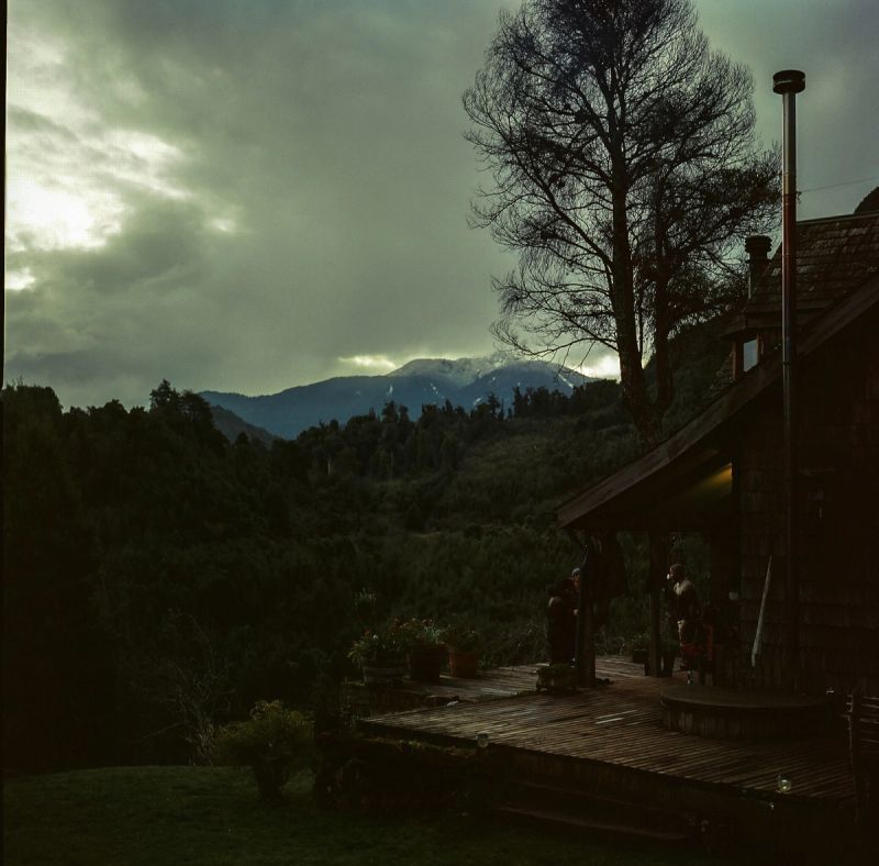 Silhouetted wooden cabin deck overlooking misty mountains and forest in Patagonia, Chile.