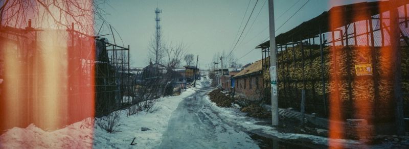 Snowy rural road with rustic buildings and stacked corn in winter landscape
