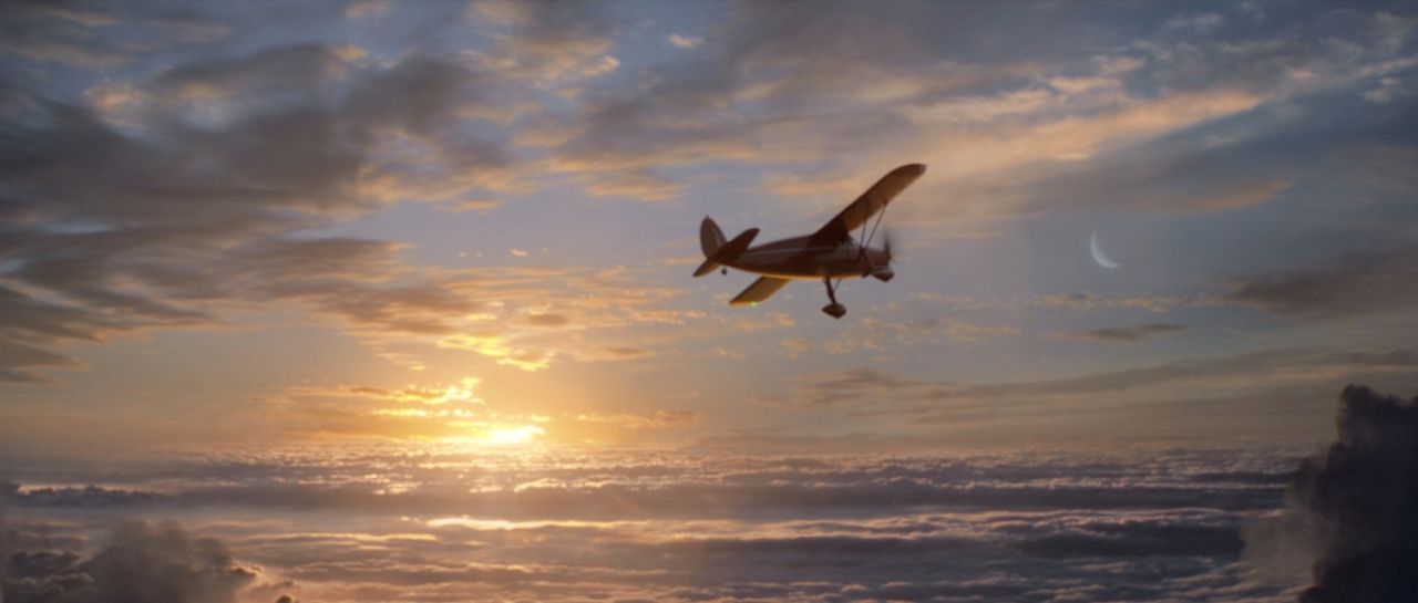 Vintage airplane flying over clouds at sunset with crescent moon
