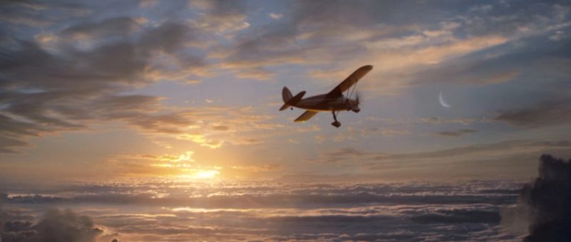 Vintage airplane flying over clouds at sunset with crescent moon