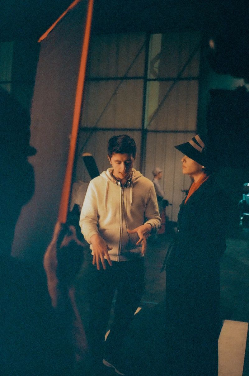 Ian Rigby directing Andrew De Zen on a dimly lit film set with large lighting equipment.