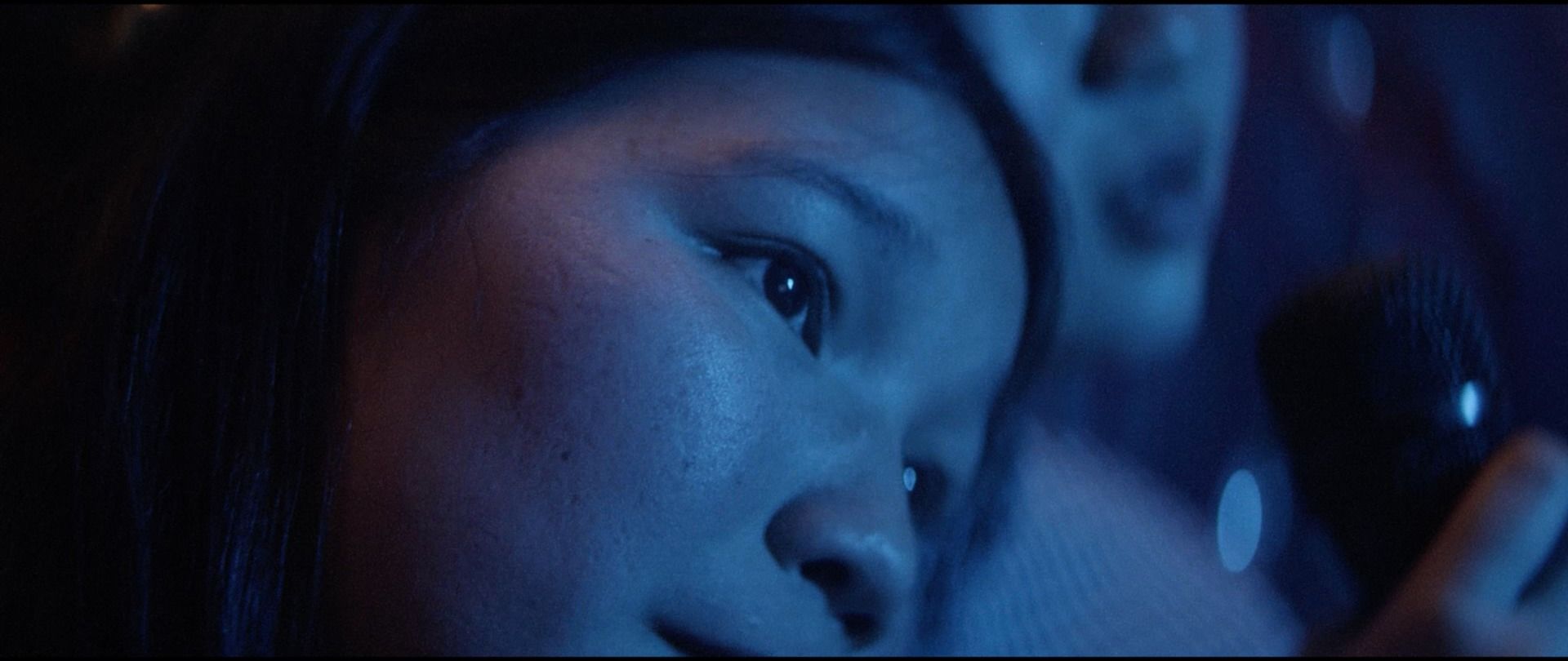 Close-up of a woman's face in blue-toned cinematic lighting, holding a microphone.