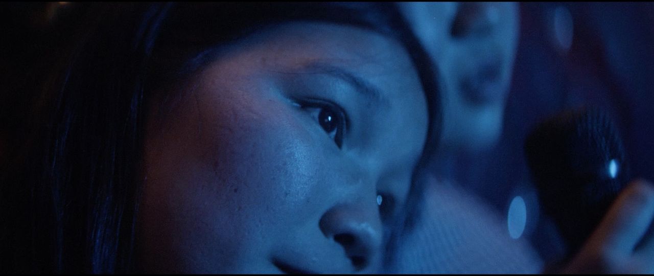 Close-up of a woman's face in blue-toned cinematic lighting, holding a microphone.