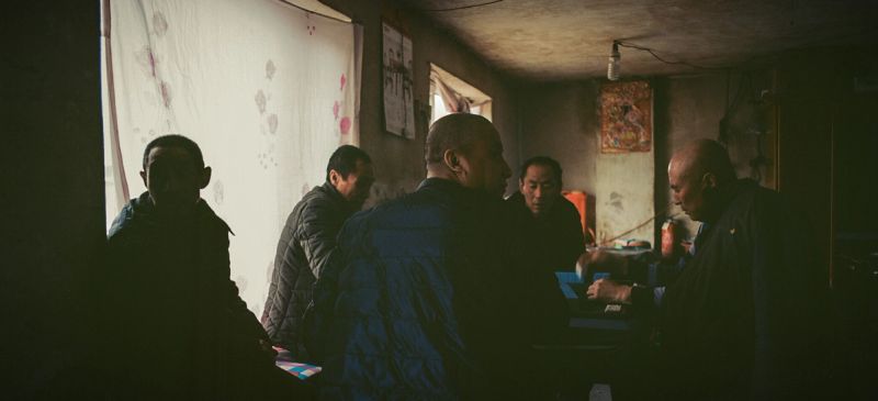 Five men in dimly lit room, one man seated at table with papers