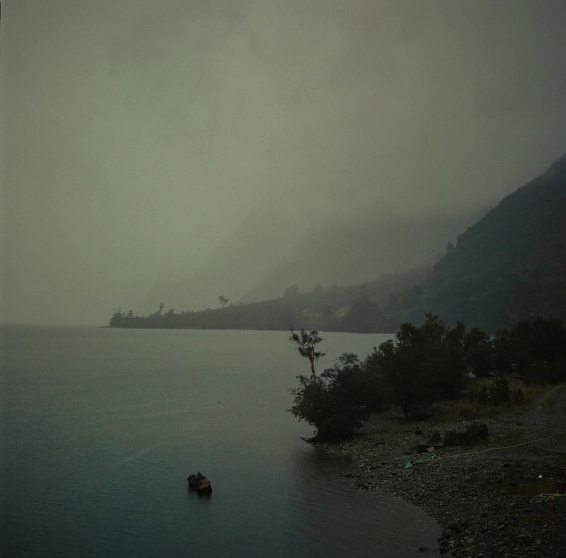 Misty lake landscape in Patagonia Chile with mountains fading into fog and rocky shoreline.