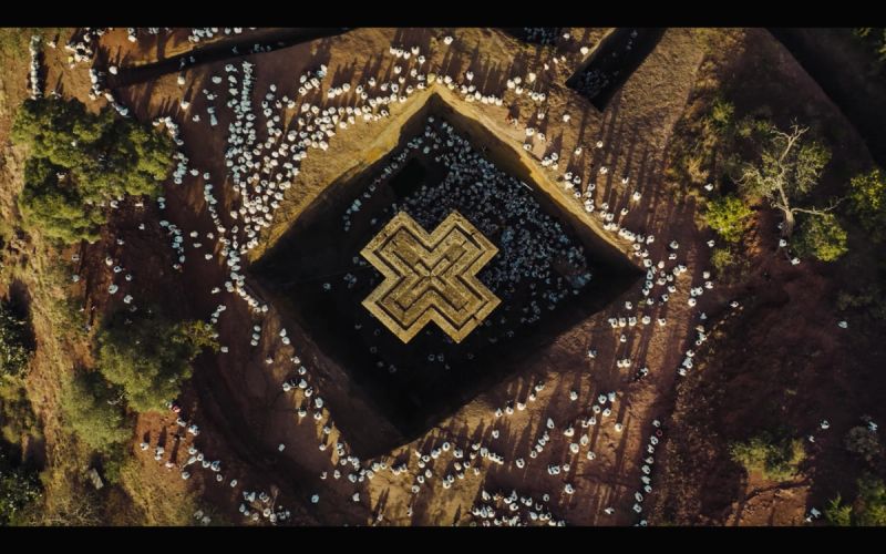 Aerial view of a large crowd gathered around a square rock-hewn church in Ethiopia.