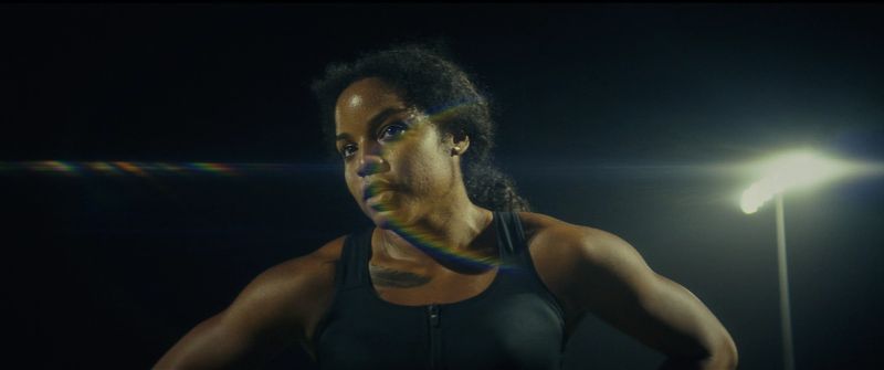 Jen Welter looks intense under dramatic stadium lights and rainbow lens flare during a women's football night shoot.