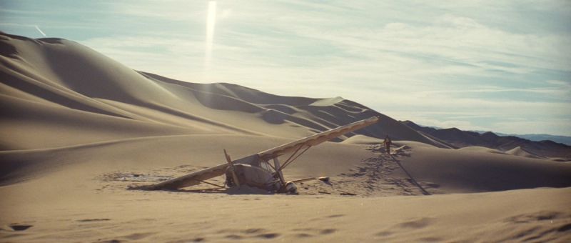 Crashed biplane in vast desert dunes under bright sun