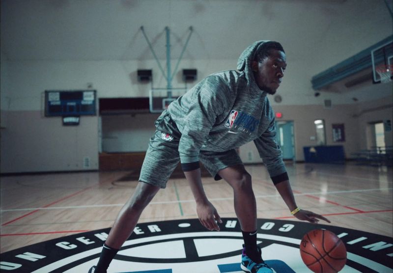 Reggie Jackson dribbling a basketball on an indoor court wearing a grey hoodie.