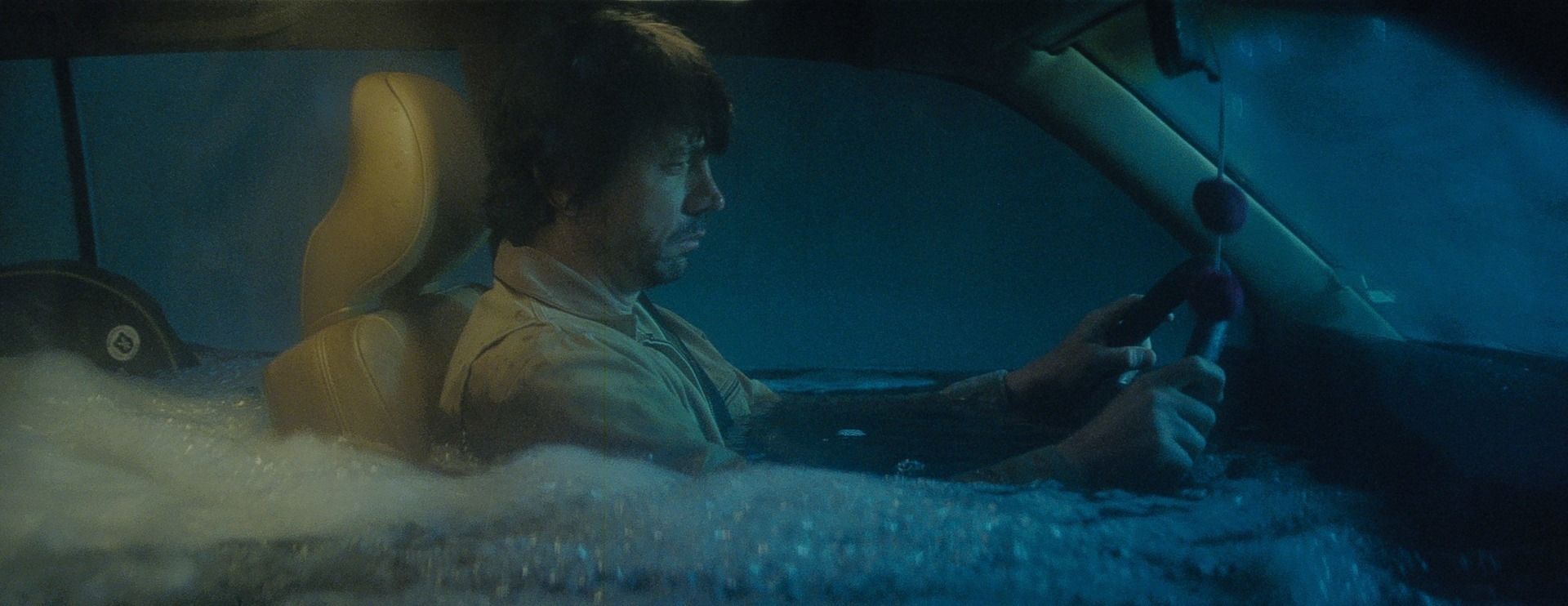 Actor submerged in water inside a car, holding steering wheel
