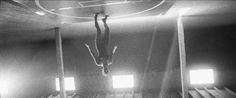 Olympic wrestler hanging upside down from gymnasium ceiling in black and white film photography.