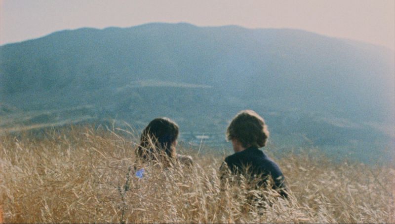 Two people sit in tall grass overlooking hazy mountain landscape