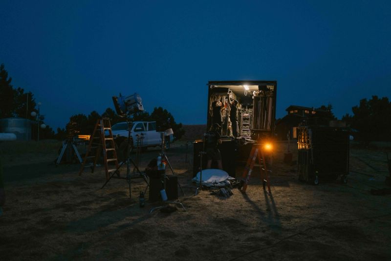 Crew setting up lighting equipment on a film set at dusk in the mountains