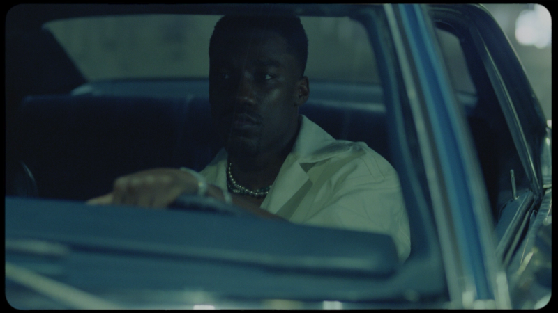 Giveon in a vintage car, wearing a white shirt and pearl necklace, cinematic film photography.