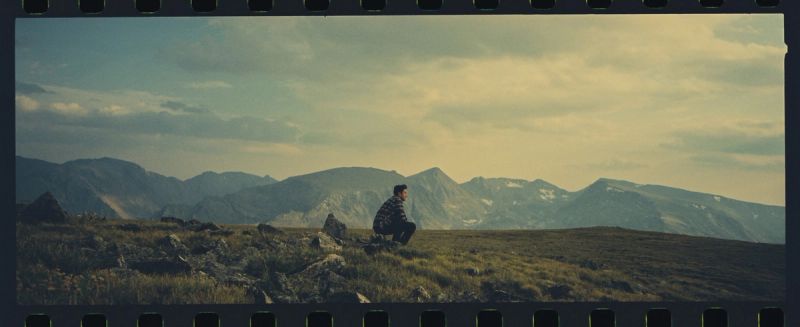 A lone figure sits on a grassy ridge overlooking Colorado mountains, shot on Kodak Portra 400 with a Hasselblad XPan.