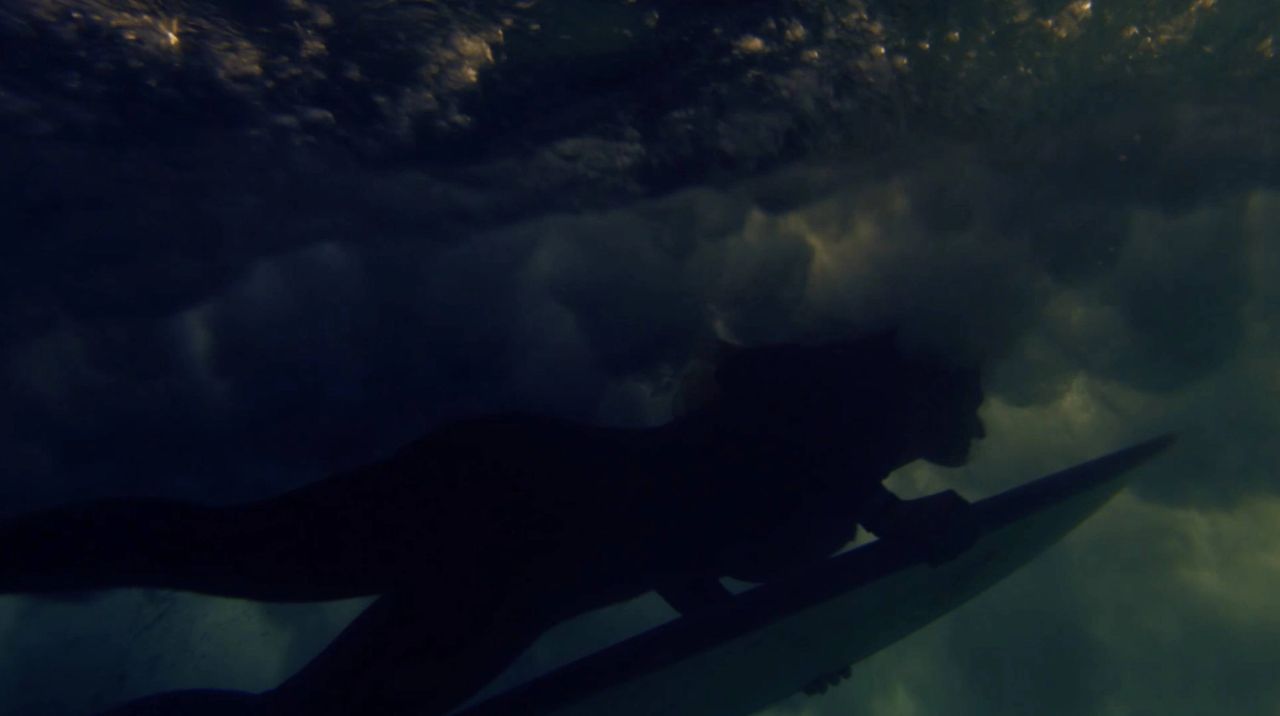 Surfer paddling underwater beneath a breaking wave