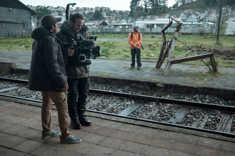 Cinematographer operating camera on train platform during commercial film shoot with actor.