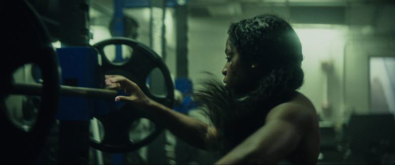Woman reaching for a barbell in a gym during the EastBay ConqHer Santia Deck project.
