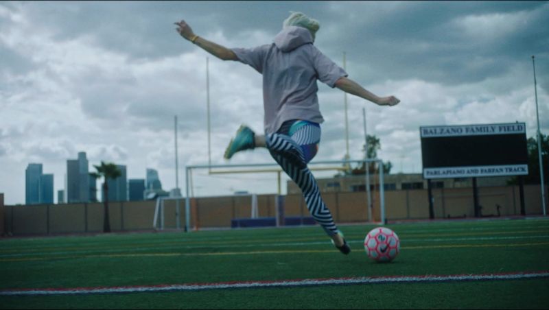 Athlete kicks soccer ball on field with city skyline in background