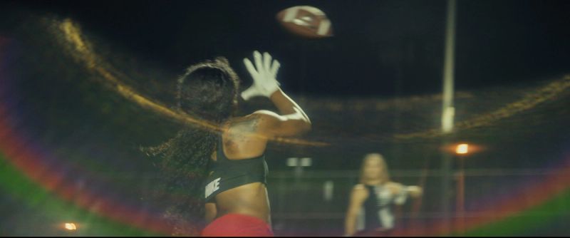 Jen Welter reaching for a football catch at night in the Eastbay ConqHer Santia Deck campaign.