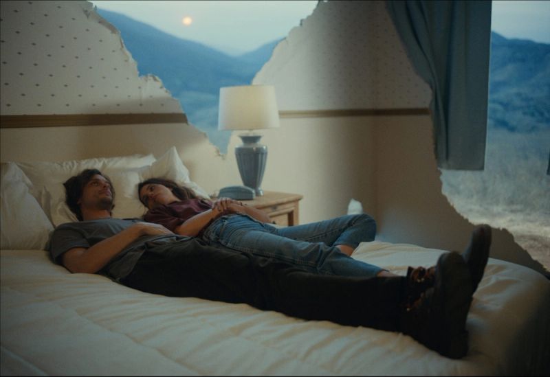 Couple lying on bed with torn wall revealing mountain view at dusk