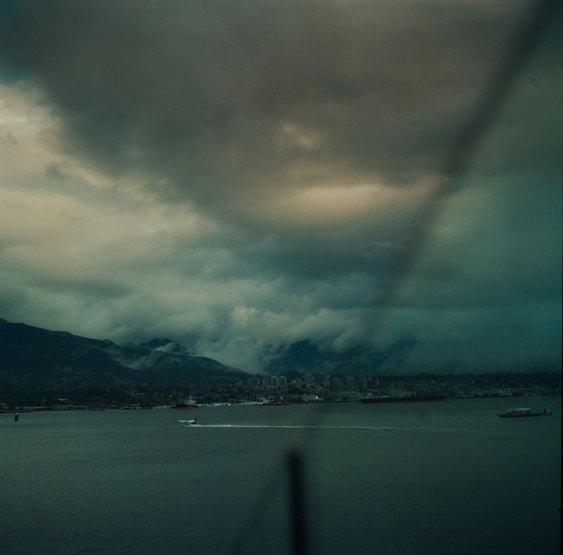 Stormy coastal cityscape with mountains under dark clouds and water below