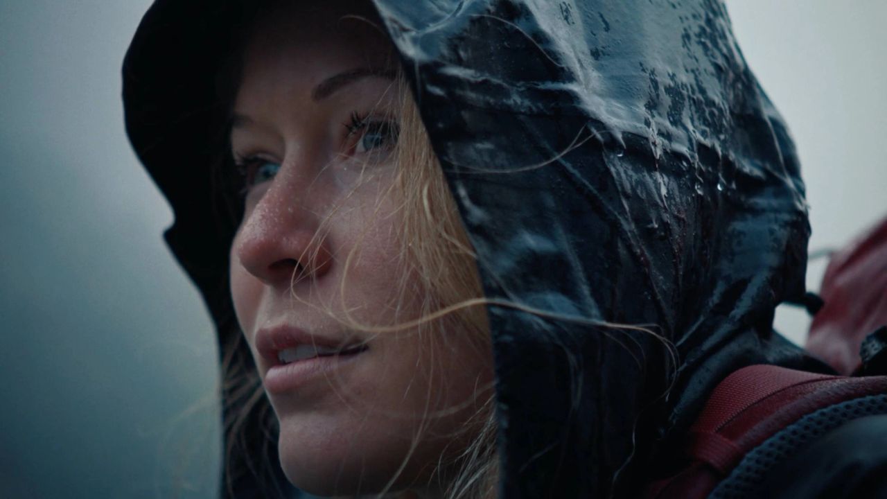 Close-up portrait of a woman in a soaked rain hood looking off-camera during a storm.