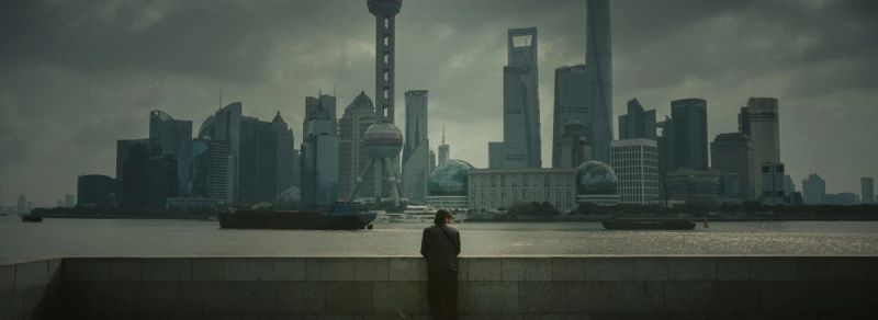 Cinematography shot of a lone figure standing on a wall overlooking the Shanghai skyline and river.