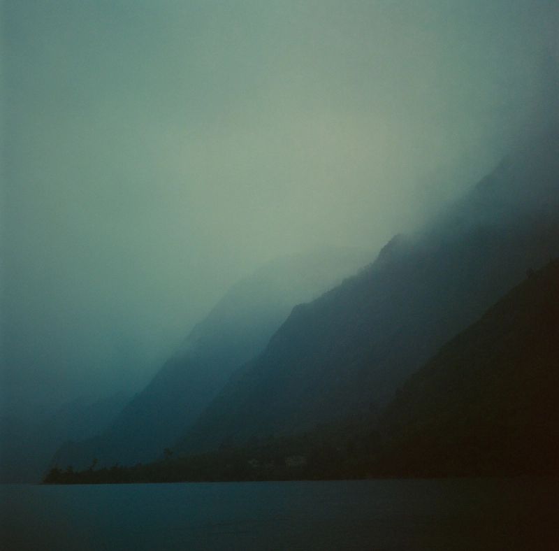 Atmospheric misty mountain slope descending to water in foggy Patagonia landscape. Film photography.