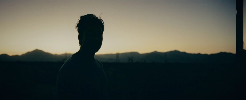 Silhouette of a person standing before mountains at twilight, film photography.