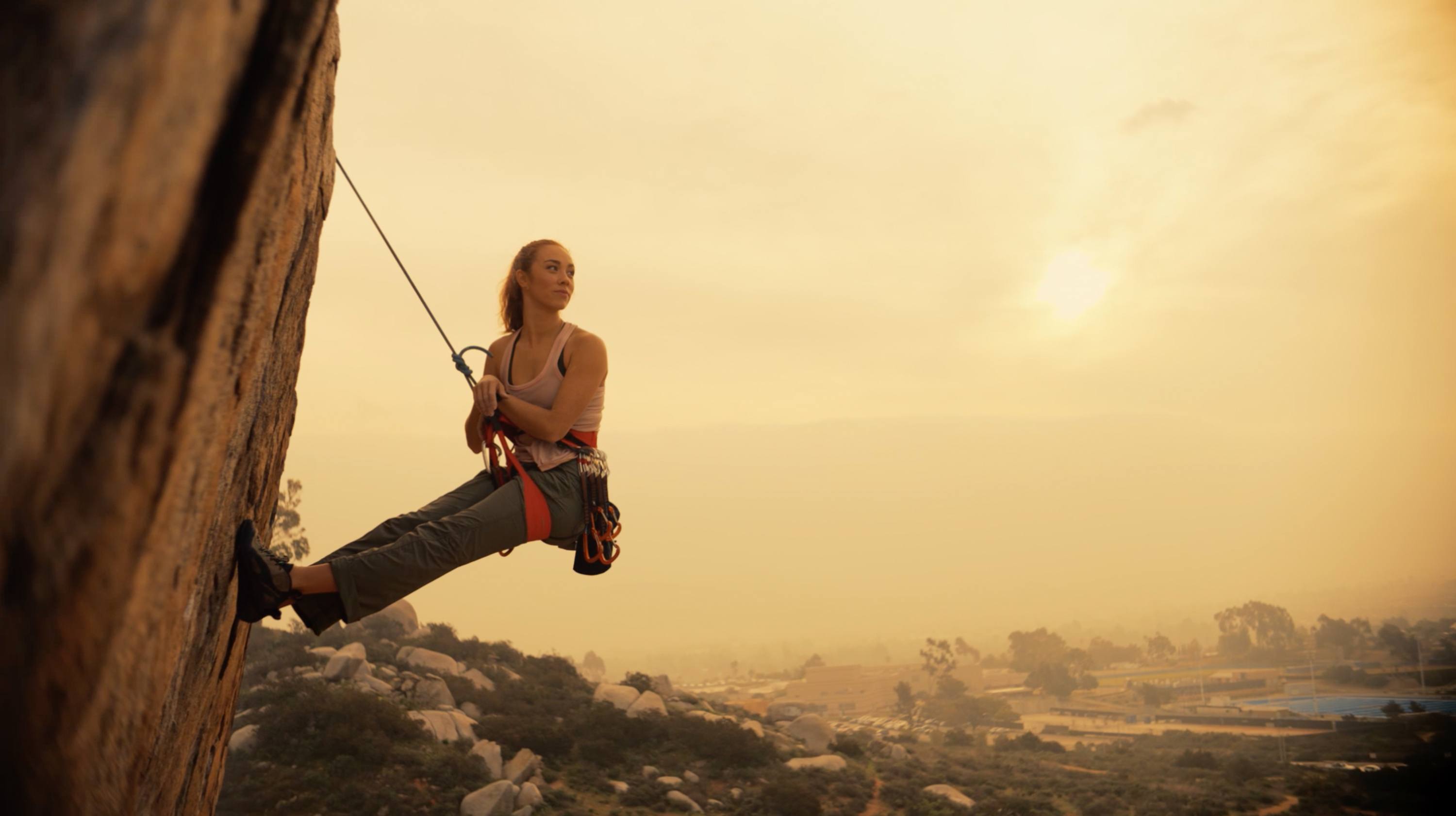 Female climber rappelling on rock face at golden hour