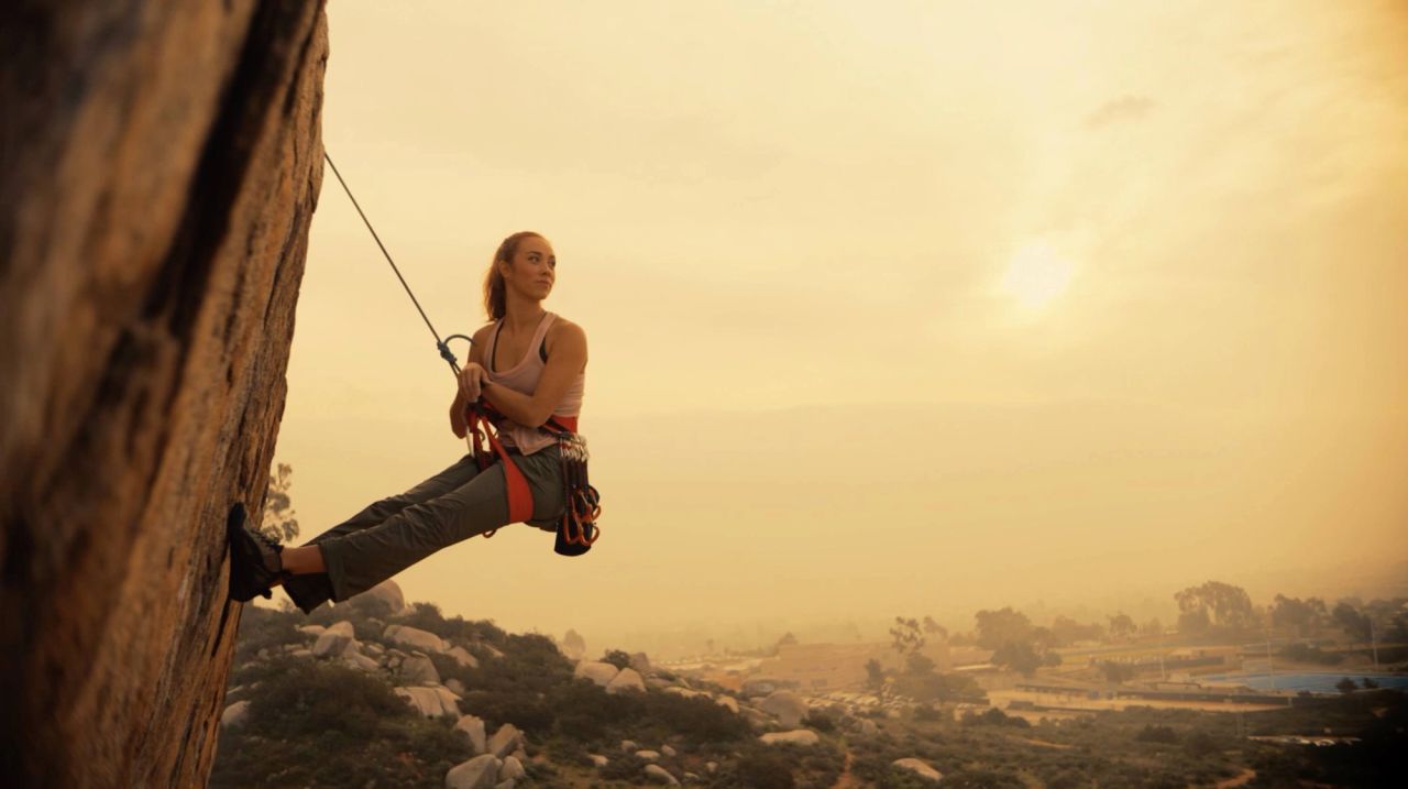 Female climber rappelling on rock face at golden hour