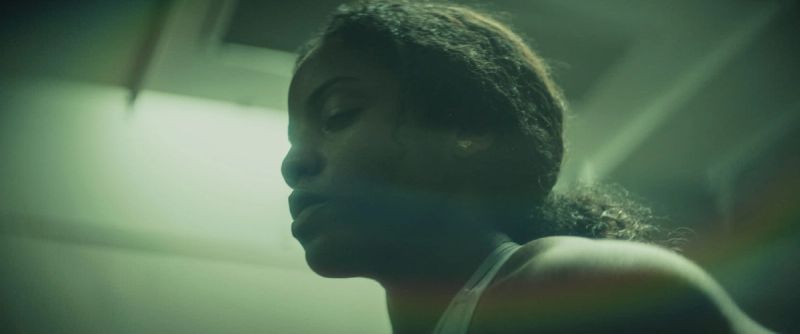 Female athlete in profile with eyes closed under moody green lighting.