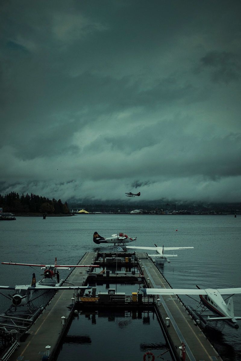 Seaplanes docked at a marina under moody, overcast skies with one plane taking off.