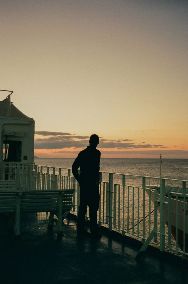 Silhouette of a person standing on a boat deck overlooking the ocean at sunset.