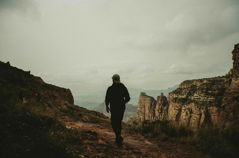 Hiker walking on a rocky trail overlooking dramatic cliff formations in an Ethiopian landscape.