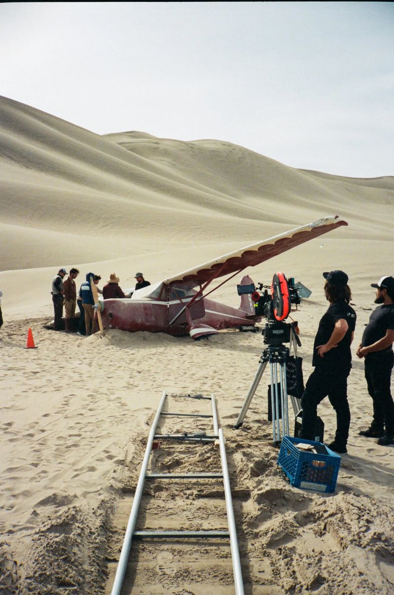 Film crew on sand dunes with vintage plane and camera gear
