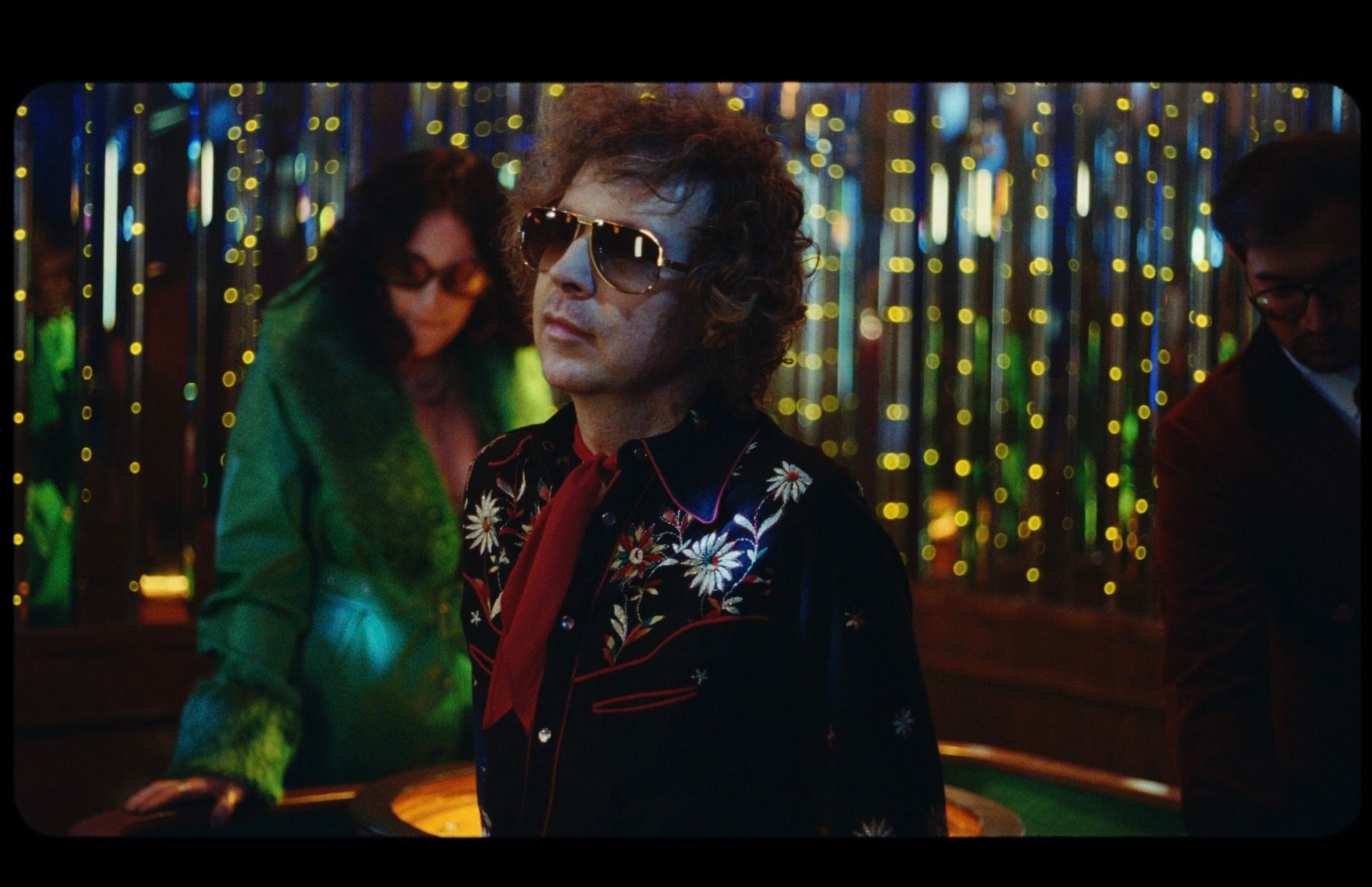 Orville Peck in floral shirt and sunglasses at a casino table with colorful lights