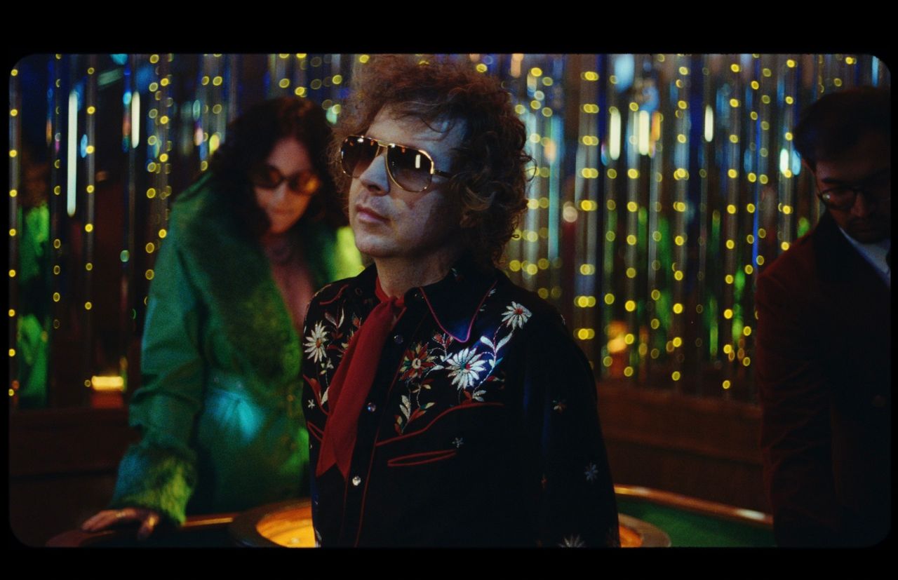 Orville Peck in floral shirt and sunglasses at a casino table with colorful lights