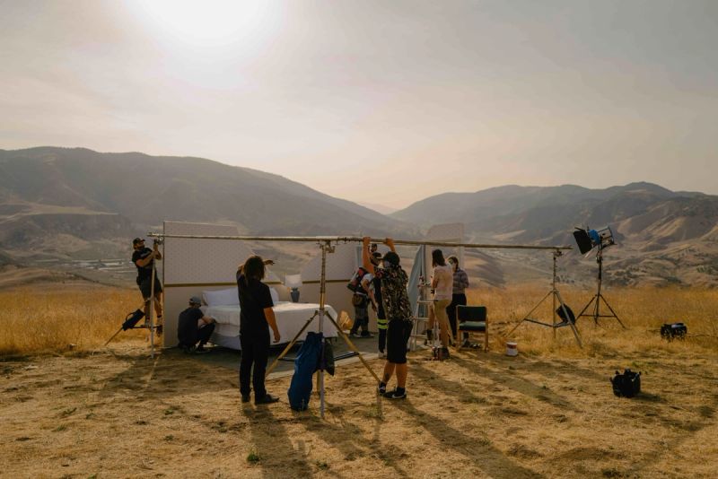 Crew sets up outdoor bedroom scene on mountain ridge with lighting and backdrop