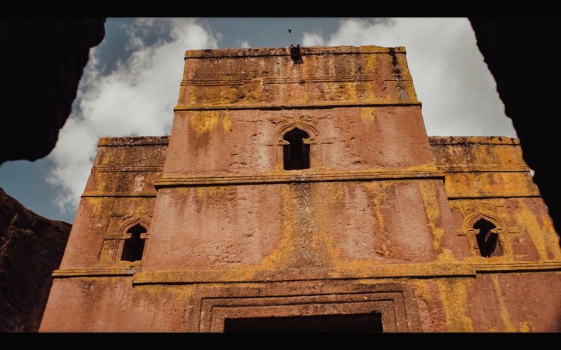 Ancient rock-hewn church facade with arched windows and weathered stone texture under cloudy sky