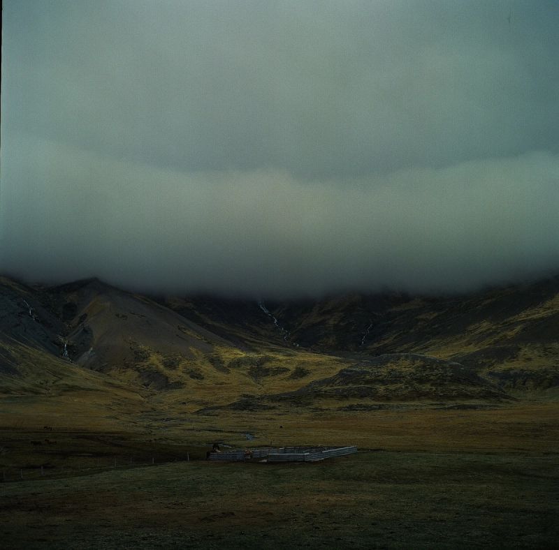 Moody Icelandic highlands landscape with mist-covered mountains and a fenced enclosure in the foreground.