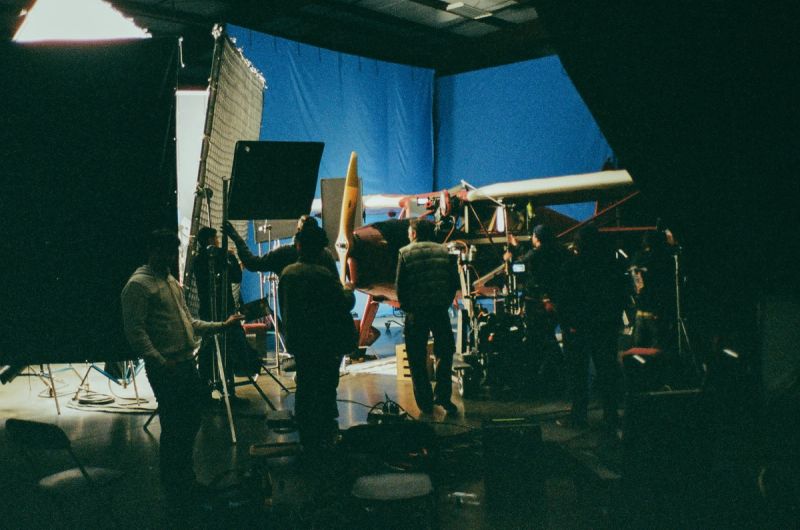 Crew on film set with vintage airplane under blue screen lighting