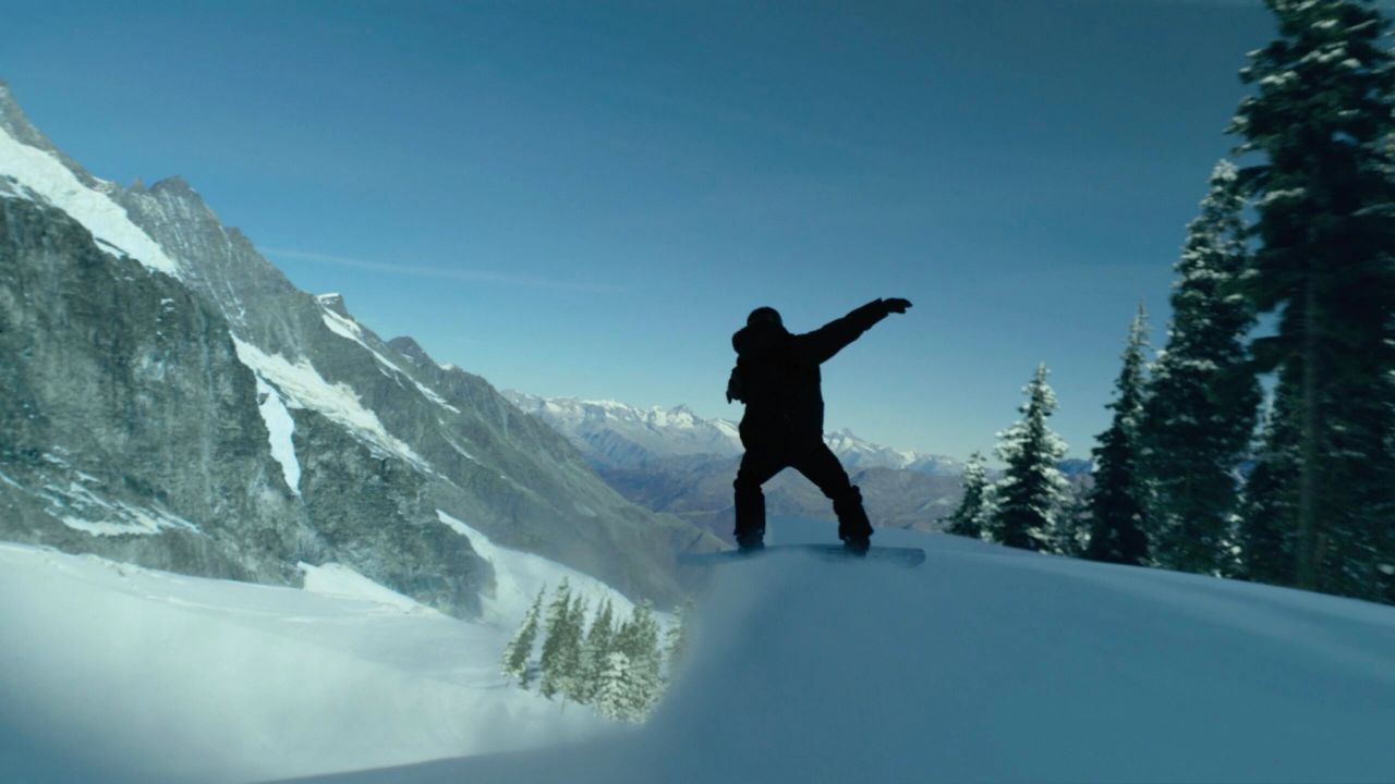 Snowboarder silhouetted against snowy mountain ridge under clear blue sky