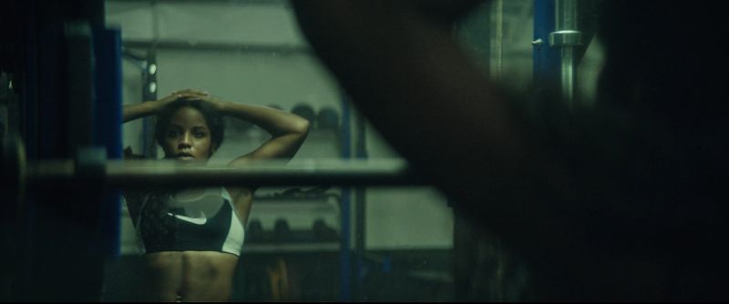 Jen Welter looking into a gym mirror with hands behind head during the EastBay ConqHer campaign.
