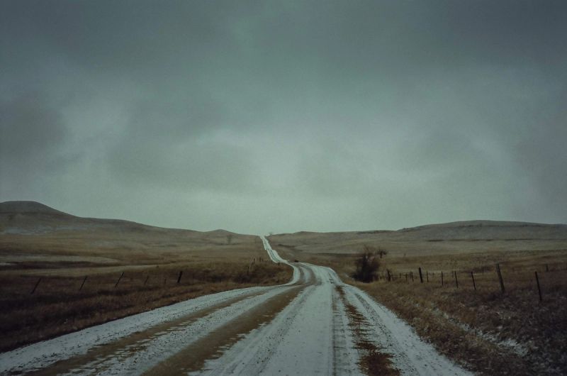 Snow-dusted dirt road winding through open Montana hills under overcast sky
