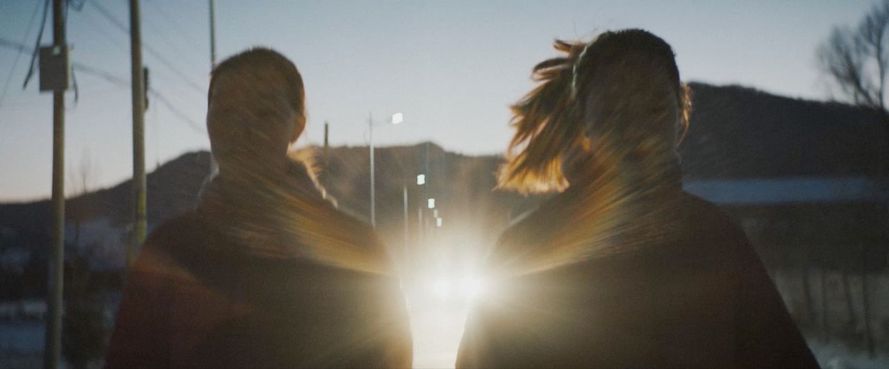 Two figures walking into bright light with motion blur in mountainous landscape