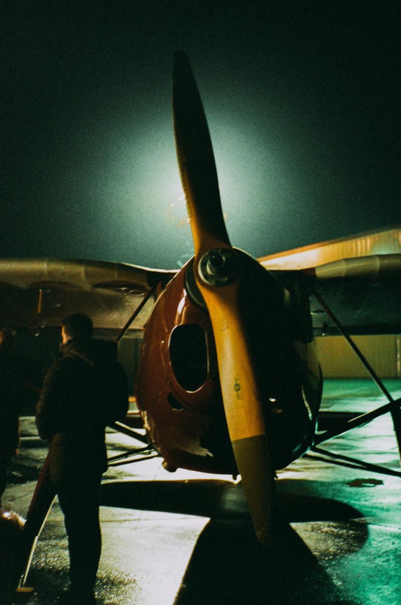 Nighttime film photography of vintage propeller plane with crew on tarmac
